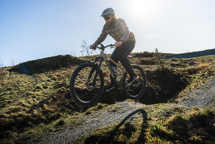 Billedet viser en mand der cykler på e-mtb i et kuperet terræn.